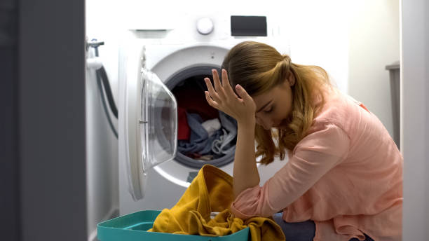 istock Tired woman loading clothes in washing machine, annoyed with housework routine 1183329451