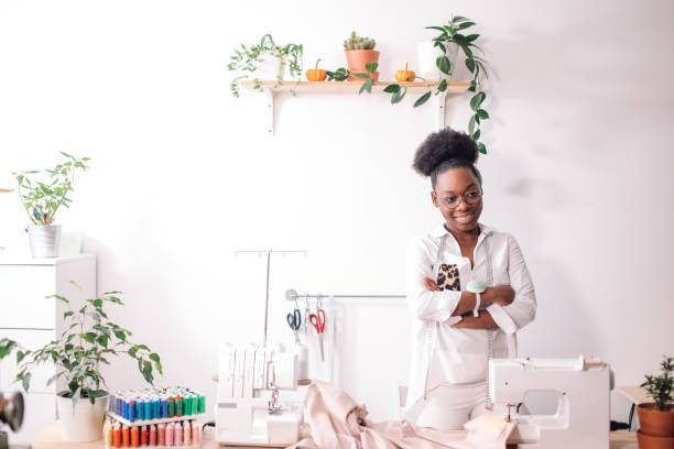 istock smiling seamstress looking at camera with sewing machine 1183329814