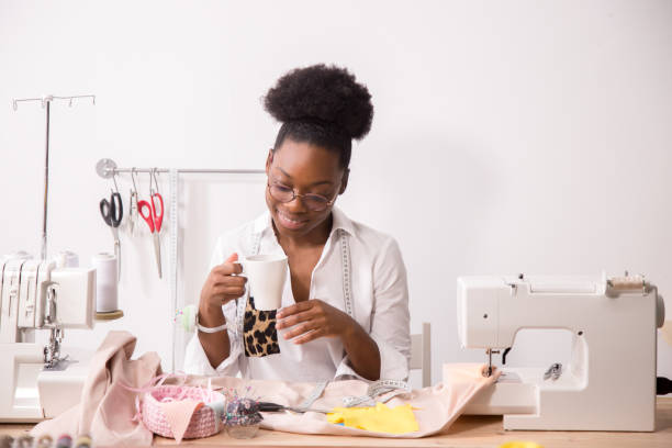 istock Cheerful woman seamstress in apron talking on phone and drinking coffee 1183335607