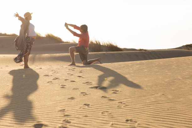 istock Smiling woman posing on sand while her husband photographing 1183337022