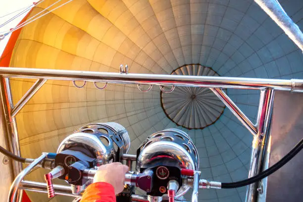 Hot air balloon flight. Close up view inside the dome of aerostat. Hand of pilot or captain holding gas-burner from which the flame escapes.