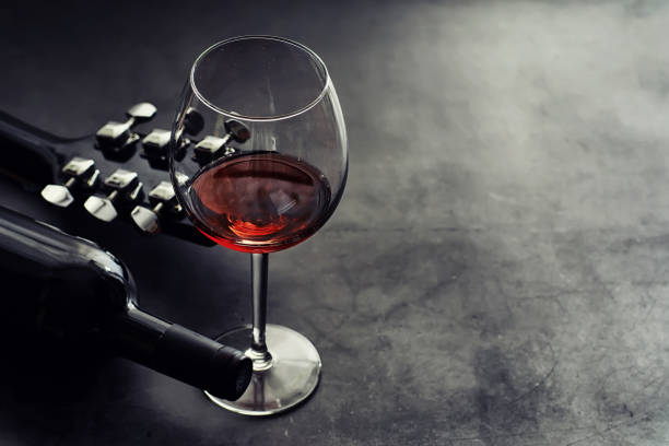 Guitar and high glass with red wine on a stone background.