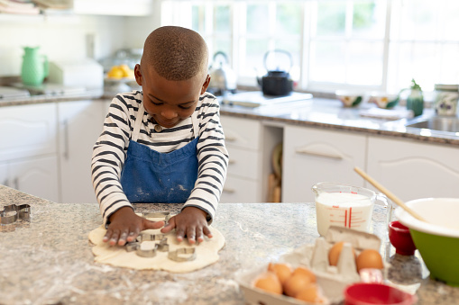Front view of a young mixed race boy in a kitchen at Christmas, making cookies and cutting out shapes