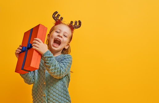 Happy little girl with Christmas gift on bright color background. Yellow, red and teal.