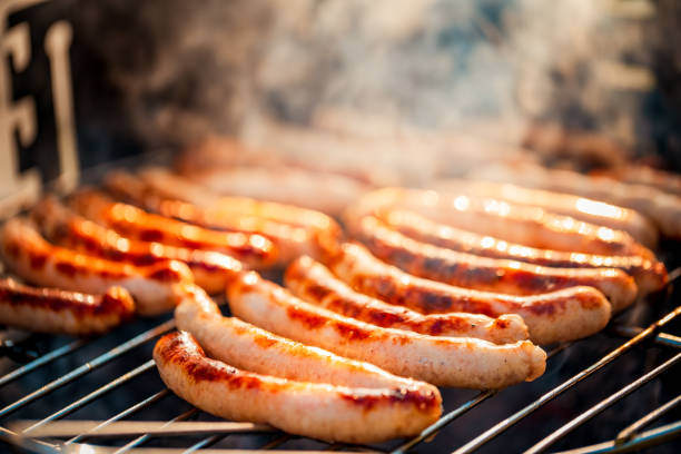 BBQ with fiery sausages on the grill outdoor picnic. Spending time together with the family at the grill. Social meetings, friends. Juicy and well-grilled sausages