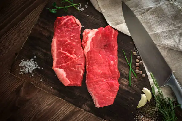 Two raw chuck steak on a wooden Board on a table prepared for the grill. Top view rustic style