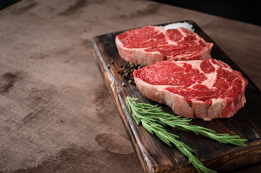 Two fresh raw rib-eye steak on wooden Board on wooden background with salt, pepper and rosmary in a rustic style