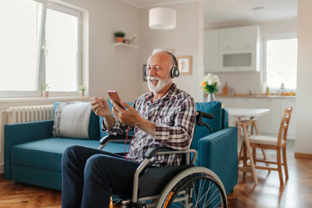 homme aîné handicapé dans un fauteuil roulant utilisant le smartphone et les écouteurs - men smiling headphones individuality photos et images de collection