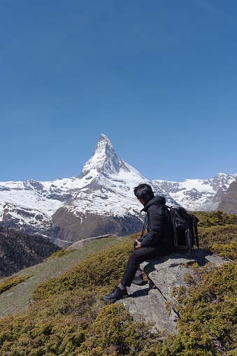 a man with backpack sitting on rock with Matterhorn mountain view in Switzerland. Travel lifestyle and adventurous