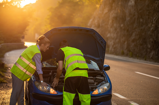 Young woman receiving roadside assistance from a young man after breaking down on the road