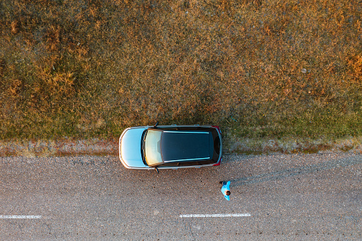 Woman and car on road through grassy wastelands, aerial view directly above from drone pov