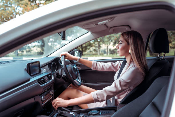 Beautiful girl business lady, summer city, rides car interior. Tanned skin, formal suit long hair casual makeup. Car rental, car sharing. Right-hand drive, left-hand drive, automatic transmission. stock photo