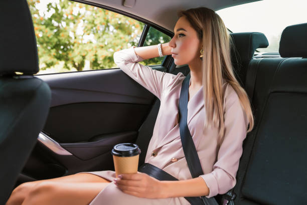 istock Beautiful woman car interior passenger, resting after work lunch, having snack cup coffee tea. Business VIP taxi rental car sharing city. Summer girl autumn city. Strict suit long hair casual makeup. 1183376545