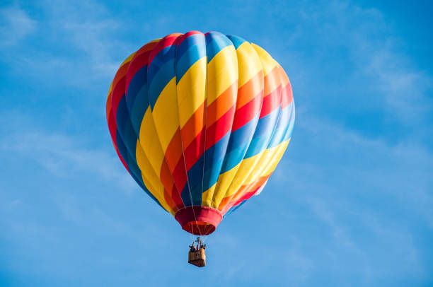 Single Hot Air Balloon Yellow, red and blue hot air balloon flying overhead in a clear blue sky. hot air balloon stock pictures, royalty-free photos & images