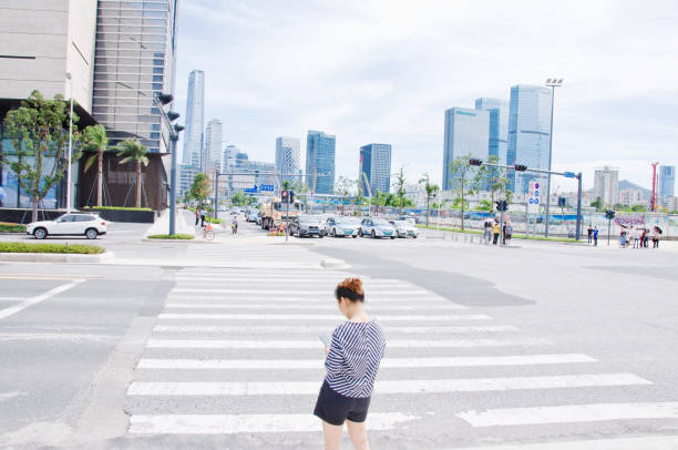 Pedestrian using a mobile while waiting to use the zebra crossing in the affluent quarters of Futian Central Business District, Shenzhen - China