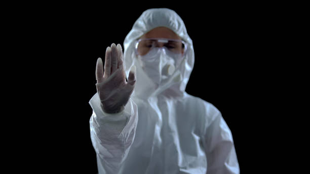 istock Woman in protective suit showing stop sign against dark background, caution 1183376826