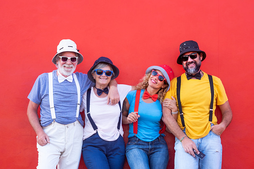 Family group in affectionate attitude. Embrace and smile against a red wall. Four people with bow ties, caps and suspenders