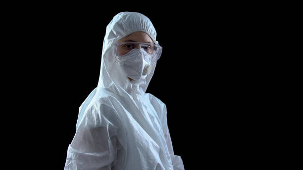 istock Lab worker in protective suit and mask looking at camera against dark background 1183376977