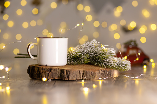 Decoration for New Year's holidays. Warm cozy atmosphere. White metal mug on a wooden stand, next to a snowy Christmas tree branch