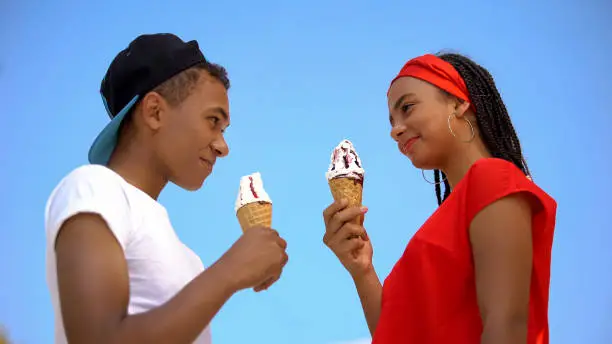 Two teenagers holding sweet ice-cream cone looking each other, bottom-view