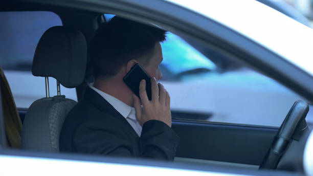 istock Secret agent spying from car, talking phone with partner, discussing information 1183382660