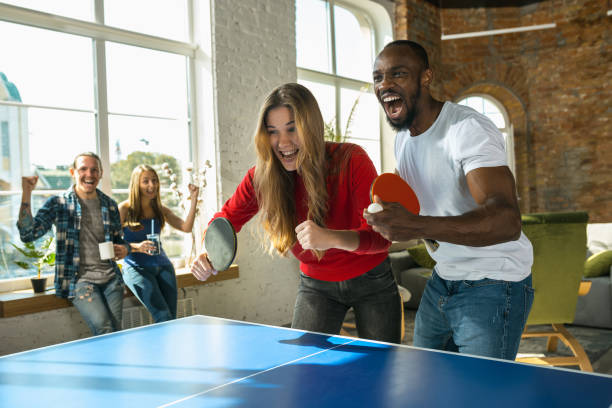 jeunes jouant au tennis de table dans le lieu de travail, ayant l'amusement - tennis indoors sport leisure games photos et images de collection
