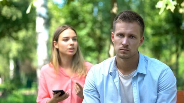 istock Sad young man looking camera, annoyed jealous girlfriend holding phone, distrust 1183389504