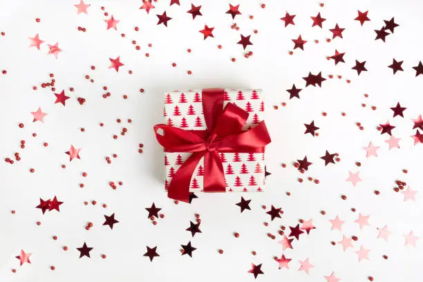 Christmas present with red bow on white background with red stars and sparkles. Xmas template. Happy. New Year. Flat lay style.
