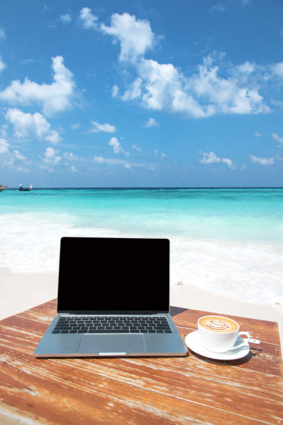 istock Laptop computer and coffee cup on the beach table 1183393641