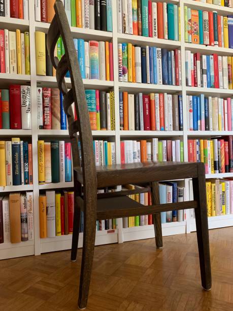 istock Multi colored books in shelves and an old wooden stool standing in front 1183395937