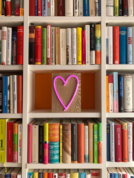 istock Multi colored books in shelves and a pink neon heart shape in empty part 1183396250