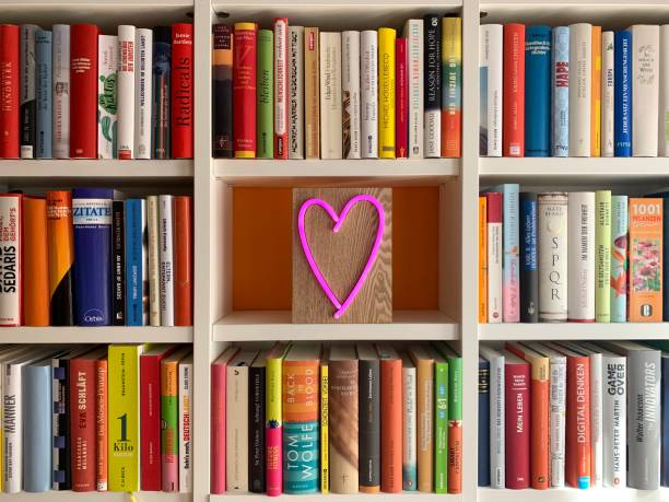 istock Multi colored books in shelves and a pink neon heart shape in empty part 1183396385