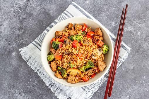 Ramen Noodles with Broccoli, Bell Pepper, Mushroom, and Chicken in a Bowl with Chopsticks Directly Above Photo.