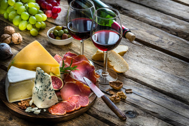 apéritif : vin rouge, fromage et jambon salé sur table en bois rustique - food appetizer still life ham photos et images de collection