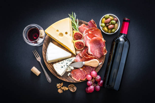 istock Appetizer: red wine, cured ham and cheese on black background 1183406627