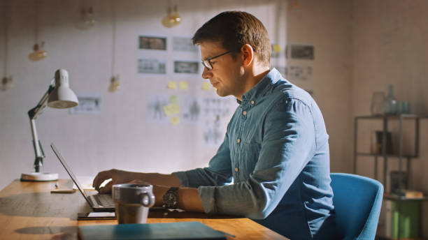 istock Professional Creative Man Sitting at His Desk in Home Office Studio Working on a Laptop. Man working with Data and Analyzing Statistics. 1183411308