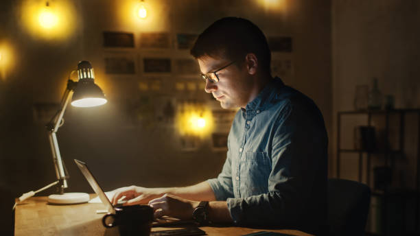 istock Concentrated Man Sitting at His Desk in Office Studio Working on a Laptop in the Evening. Work with Data, Analyzing Statistics. 1183411344