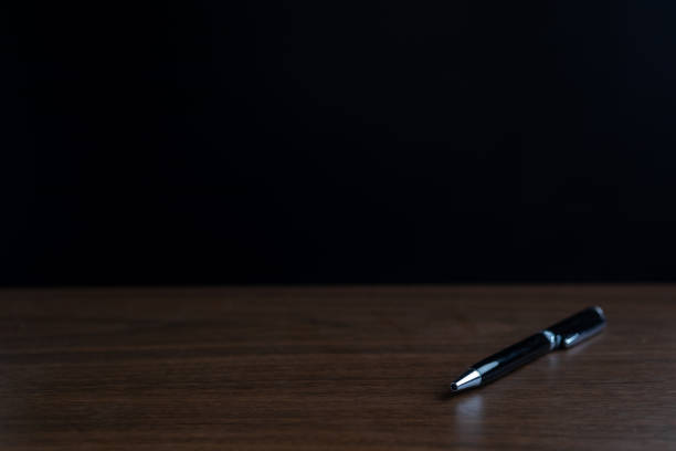 The pen is placed on a wooden table with a black background.