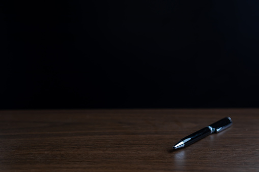 The pen is placed on a wooden table with a black background.