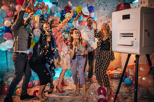 Group of young women and men having fun with balloons and photo booth at a party