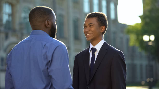 istock Afro-american father greeting son in suit outdoors university, prom celebration 1183419663
