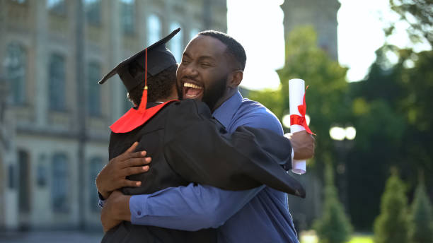 père gai et fils gradué étreignant en plein air, accomplissement d'étude, éducation - son photos et images de collection