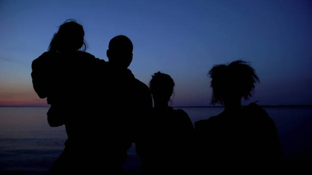 istock Family silhouette standing against night sea background, unity in difficulties 1183422060