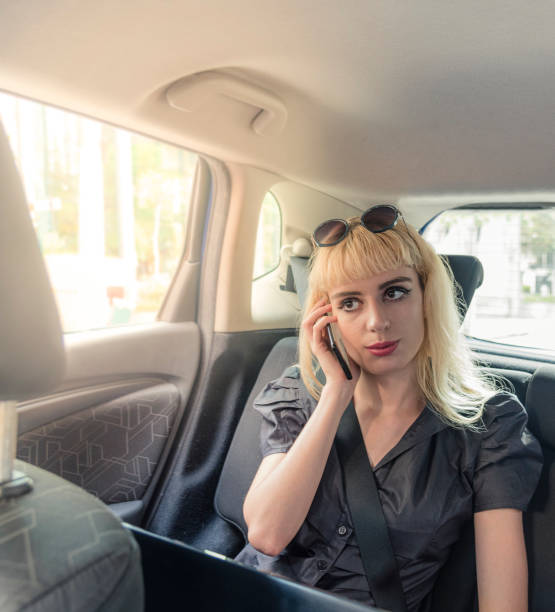 istock Young woman working on her notebook and talking on smart phone during the commute requested by taxi application - anywhere office concept 1183422112