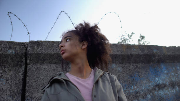 Biracial teenage girl standing behind wire fence, dreaming to escape from camp Biracial teenage girl standing behind wire fence, dreaming to escape from camp child arrest stock pictures, royalty-free photos & images