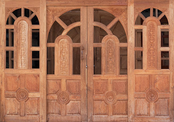 Red wooden entrance door in a tenement in Kalisz, with round glass windows, concrete facade, and yellow installation sign on the wall.