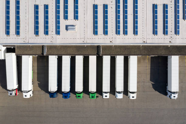 Aerial view of Semi-Trucks Loading at Logistic Center, Distribution Warehouse Aerial view of cargo containers, semi trailers, industrial warehouse, storage building and loading docks, renewable energy plants, Bavaria, Germany unloading photos stock pictures, royalty-free photos & images
