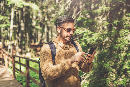Modern hipster guy holding mobile phone in nature. Travel, technology and healthy lifestyle concept.