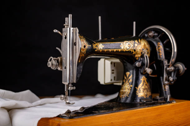 istock Old sewing machine and white material on a dark table. An antique device for small housework. Dark background. 1183436261