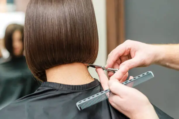 Photo of Hands of professional hair stylist is cutting hair tips with scissors and comb.